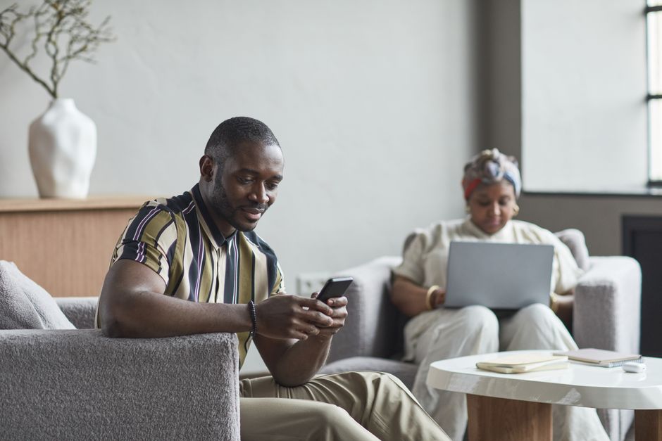 Dva hosté v hotelové lounge pracují na notebooku a telefonu připojeni k WiFi